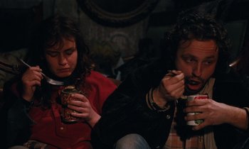 Movie still from “Vagabond” (1985), directed by Agnès Varda – A man and a woman sitting next to each other eating food; Medium shot, High angle