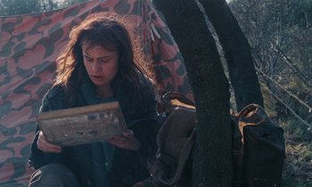 Movie still from “Vagabond” (1985), directed by Agnès Varda – A woman holding a piece of wood near a tree; Medium shot, Over the shoulder angle