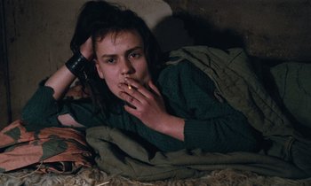 Movie still from “Vagabond” (1985), directed by Agnès Varda – A person laying on the ground with a cigarette in their mouth; Close Up shot, High angle