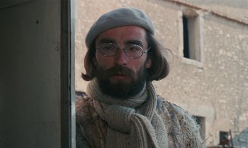 Movie still from “Vagabond” (1985), directed by Agnès Varda – A man with a beard wearing glasses and a hat; Close Up shot, Over the shoulder angle