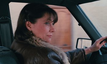Movie still from “Vagabond” (1985), directed by Agnès Varda – A woman sitting in the drivers seat of a car; Close Up shot, Over the shoulder angle