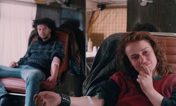 Movie still from “Vagabond” (1985), directed by Agnès Varda – A woman sitting in a chair with a blood bag on her arm and a man sitting in a chair with a blood bag on his arm; Medium shot, High angle
