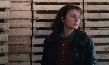 Movie still from “Vagabond” (1985), directed by Agnès Varda – A woman standing in front of a wall of wooden pallets; Close Up shot, Over the shoulder angle
