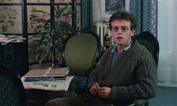 Movie still from “Vagabond” (1985), directed by Agnès Varda – A man sitting on a chair in a room; Medium shot, High angle