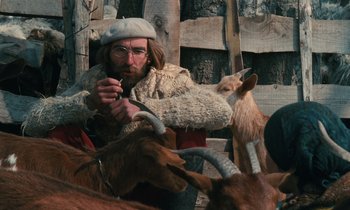 Movie still from “Vagabond” (1985), directed by Agnès Varda – A bearded man wearing a hat and holding a stick with two goats in front of him; Medium shot, Low angle