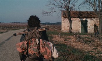 Movie still from “Vagabond” (1985), directed by Agnès Varda – A person with a backpack walking in a field; Wide shot, Over the shoulder angle