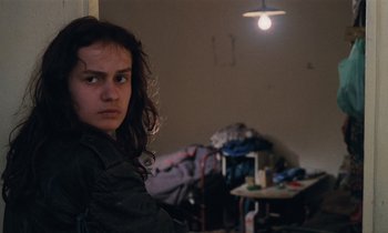 Movie still from “Vagabond” (1985), directed by Agnès Varda – A young woman is sitting in a messy room; Close Up shot, Over the shoulder angle