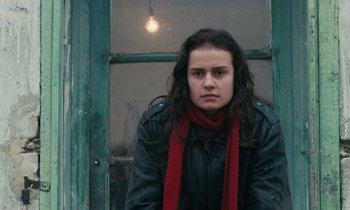 Movie still from “Vagabond” (1985), directed by Agnès Varda – A young woman wearing a red scarf standing in front of a window; Close Up shot, Low angle