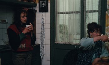 Movie still from “Vagabond” (1985), directed by Agnès Varda – Two people standing in front of a window eating food; Medium shot, Over the shoulder angle