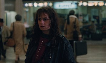Movie still from “Vagabond” (1985), directed by Agnès Varda – A woman in a leather jacket standing next to luggage; Close Up shot, Over the shoulder angle