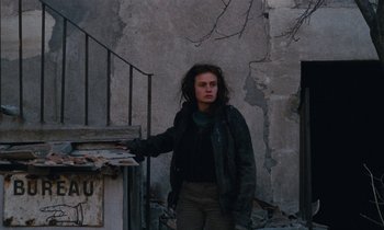 Movie still from “Vagabond” (1985), directed by Agnès Varda – A woman standing in front of an old building; Medium shot, Low angle