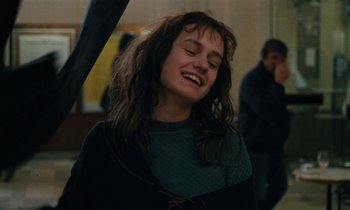 Movie still from “Vagabond” (1985), directed by Agnès Varda – A woman with long brown hair is smiling; Close Up shot, Over the shoulder angle