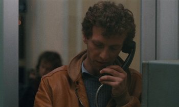 Movie still from “Vagabond” (1985), directed by Agnès Varda – A man talking on a phone while wearing a brown jacket; Close Up shot, Over the shoulder angle