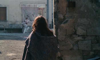 Movie still from “Vagabond” (1985), directed by Agnès Varda – A woman is walking down the street with a blanket over her head; Wide shot, Over the shoulder angle