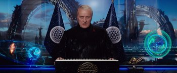 Movie still from “Valerian and the City of a Thousand Planets” (2017), directed by Luc Besson – A man in a black jacket standing in front of two flags; Medium shot, Low angle