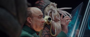 Movie still from “Valerian and the City of a Thousand Planets” (2017), directed by Luc Besson – A bald man with a beard and a green shirt is in front of an octopus statue; Close Up shot, Over the shoulder angle