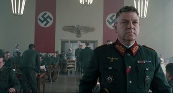 Movie still from “Valkyrie” (2008), directed by Bryan Singer – A man in military uniform standing in front of a group of people; Medium shot, Low angle