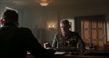 Movie still from “Valkyrie” (2008), directed by Bryan Singer – A man in a military uniform sitting at a table; Medium shot, Over the shoulder angle