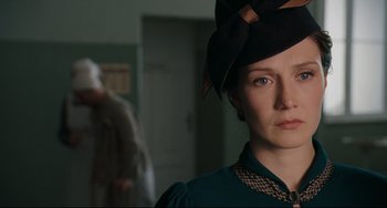 Movie still from “Valkyrie” (2008), directed by Bryan Singer – A woman wearing a hat in a room with other people; Close Up shot, Over the shoulder angle