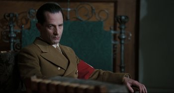 Movie still from “Valkyrie” (2008), directed by Bryan Singer – A man in a military uniform sitting in a chair; Medium shot, Over the shoulder angle