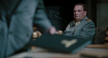 Movie still from “Valkyrie” (2008), directed by Bryan Singer – An older man in a military uniform sitting in front of a table; Medium shot, Over the shoulder angle