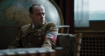 Movie still from “Valkyrie” (2008), directed by Bryan Singer – A man sitting in a chair wearing a military uniform; Medium shot, Over the shoulder angle