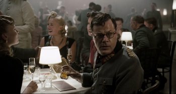 Movie still from “Valkyrie” (2008), directed by Bryan Singer – A man sitting at a table with a glass of wine; Medium shot, Over the shoulder angle