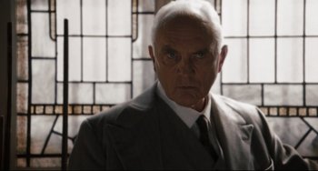 Movie still from “Valkyrie” (2008), directed by Bryan Singer – An older man wearing a suit and tie in front of a stained glass window; Close Up shot, Low angle