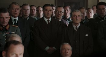 Movie still from “Valkyrie” (2008), directed by Bryan Singer – A group of men in suits and ties standing in a room; Medium shot, Over the shoulder angle