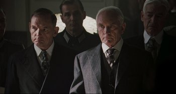 Movie still from “Valkyrie” (2008), directed by Bryan Singer – A man in a suit and tie standing next to another man in a suit and tie; Medium shot, Low angle