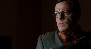 Movie still from “Valkyrie” (2008), directed by Bryan Singer – A person wearing glasses and a uniform; Close Up shot, Over the shoulder angle