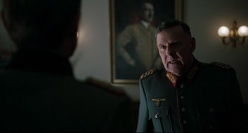 Movie still from “Valkyrie” (2008), directed by Bryan Singer – An older man in a military uniform in front of a portrait of adolf hitler; Medium shot, Low angle