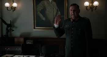 Movie still from “Valkyrie” (2008), directed by Bryan Singer – An old man in a uniform waving at the camera in front of a portrait of a nazi soldier; Medium shot, Low angle