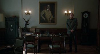 Movie still from “Valkyrie” (2008), directed by Bryan Singer – A man standing in front of a table in front of a painting of adolf hitler; Wide shot, Low angle