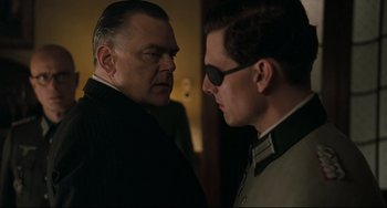 Movie still from “Valkyrie” (2008), directed by Bryan Singer – A man in a suit and sunglasses talking to another man in a suit and sunglasses; Close Up shot, Over the shoulder angle