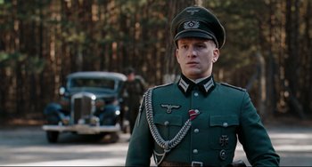 Movie still from “Valkyrie” (2008), directed by Bryan Singer – A man in a uniform standing in front of an old car; Medium shot, Low angle
