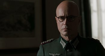 Movie still from “Valkyrie” (2008), directed by Bryan Singer – A bald man in a green uniform and glasses; Close Up shot, Low angle