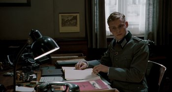 Movie still from “Valkyrie” (2008), directed by Bryan Singer – A man in a uniform sitting at a desk writing; Medium shot, Low angle