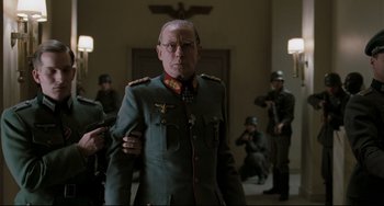 Movie still from “Valkyrie” (2008), directed by Bryan Singer – An older man in a uniform is standing in front of a group of soldiers; Medium shot, Over the shoulder angle