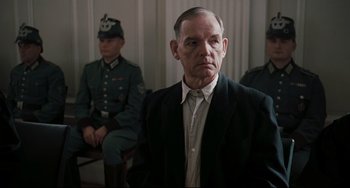 Movie still from “Valkyrie” (2008), directed by Bryan Singer – An older man in a suit and tie in front of two other men in uniform; Medium shot, Over the shoulder angle