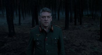 Movie still from “Valkyrie” (2008), directed by Bryan Singer – A man in a military uniform standing in the woods; Medium shot, Over the shoulder angle