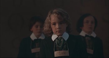 Movie still from “Velvet Goldmine” (1998), directed by Todd Haynes – A young girl wearing a neck tie and a name tag; Close Up shot, Low angle