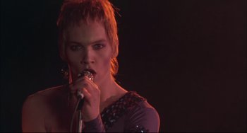 Movie still from “Velvet Goldmine” (1998), directed by Todd Haynes – A person with a microphone in a dark room; Close Up shot, Low angle