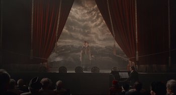 Movie still from “Velvet Goldmine” (1998), directed by Todd Haynes – A man standing on a stage in front of clouds; Extreme Wide shot, High angle