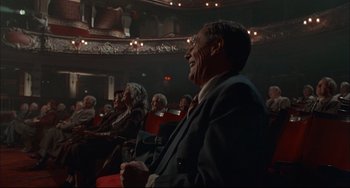 Movie still from “Velvet Goldmine” (1998), directed by Todd Haynes – An old man sitting in a theater with other old people watching; Medium shot, Low angle