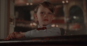 Movie still from “Velvet Goldmine” (1998), directed by Todd Haynes – A young boy wearing a white shirt and a red bow tie; Close Up shot, Low angle