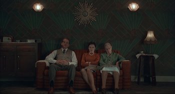 Movie still from “Velvet Goldmine” (1998), directed by Todd Haynes – A group of people sitting on top of a red couch; Wide shot, Low angle