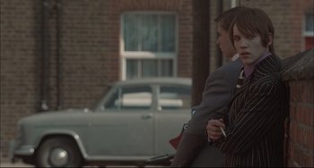 Movie still from “Velvet Goldmine” (1998), directed by Todd Haynes – A man and a woman sitting next to each other on the sidewalk; Medium shot, Over the shoulder angle