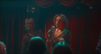 Movie still from “Velvet Goldmine” (1998), directed by Todd Haynes – Two women stand in front of a microphone on a stage; Medium shot, Low angle