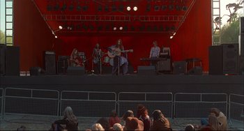 Movie still from “Velvet Goldmine” (1998), directed by Todd Haynes – A group of people sitting on a stage with a guitar; Wide shot, High angle
